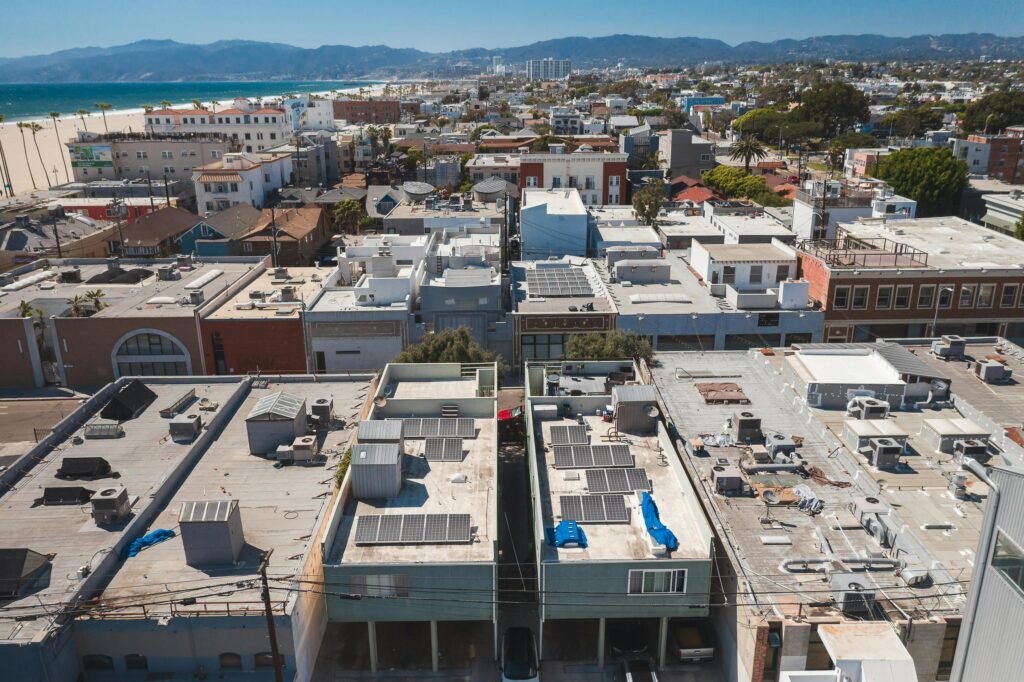 pexels-photo-8783119-8783119 Drone view of a coastal urban area with rooftops and solar panels under a clear blue sky.